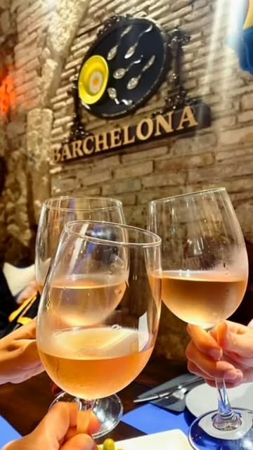 Brindis amb copes de vi davant del rètol de Barchelona i el marc de l'ou ferrat