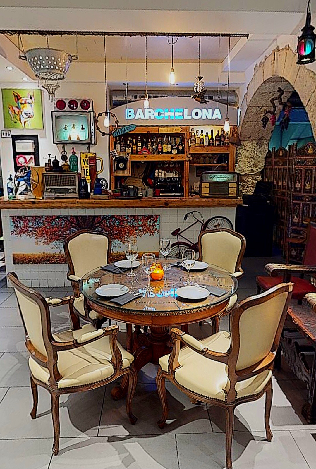 La sala de Barchelona: arc de pedra, rètol lluminós cian i cadires clàssiques al voltant d'una taula parada